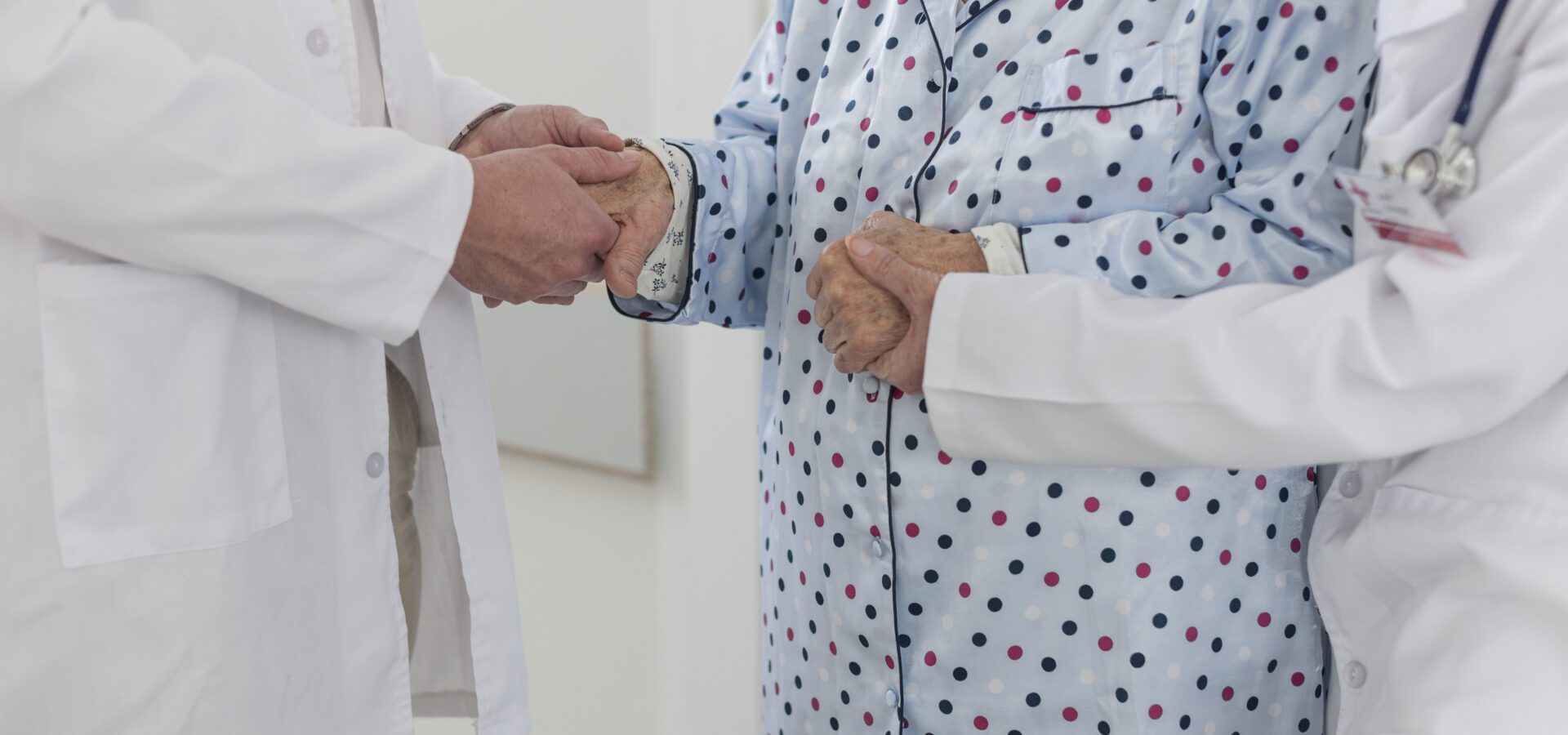 Two doctors holding hands of elderly patient